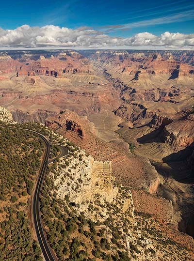 aerial view of a road through a forested area on the edge of a vast and colorful canyon