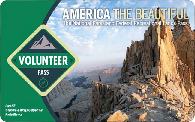 America the Beautiful 2023 Volunteer pass shows a backcountry trail ending at an overlook atop a jagged mountain peak, the words "volunteer pass" are displayed within a green diamond on the left.