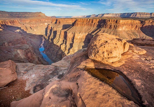 from the rim of a slickrock ledge with a water filled pothole in the foreground,