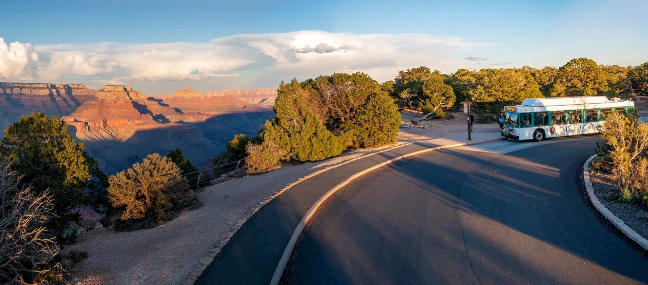 Kaibab (Orange) Route Shuttle Bus - at the Yaki Point stop. a white and green bus at a marked stop on the edge of a vast canyon landscape, just before sunset.
