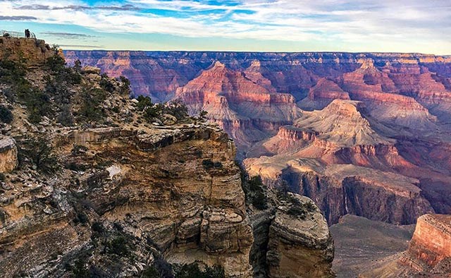 a view looking out across Grand Canyon on a sunny day with clouds in the distance.