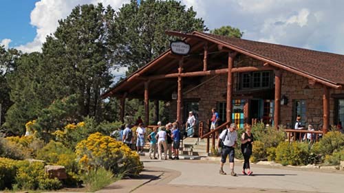 a number of people in front of historic Bright Angel Lodge in rustic style constructed of logs and stone. Yellow fall foliage.