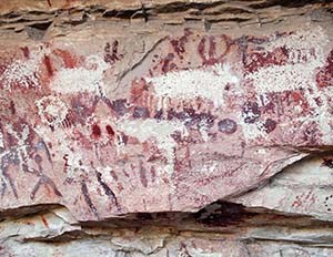 A portion of a rock art panel showing human figures painted in red and several sheep that have been chiseled over the painted designs.