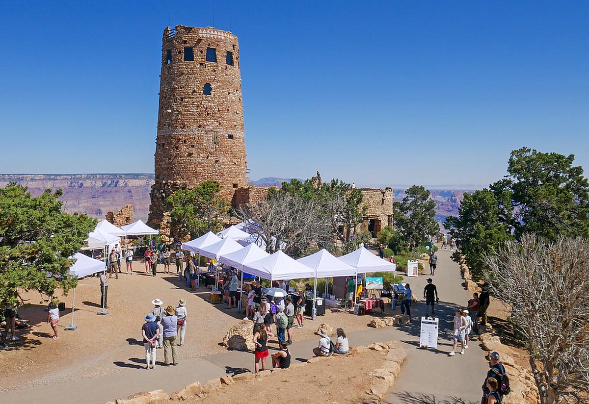 An outdoor festival with a dozen, white tent canopies at the base of a four-story stone tower.