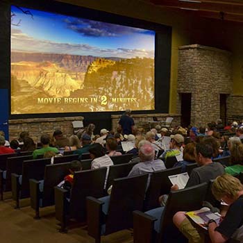 People sitting in rows of theater seats facing the screen that says, "Movie Begins in 2 Minutes."