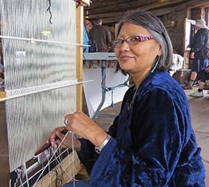 a middle aged Navajo woman sitting at a loom and beginning to weave a large rug.