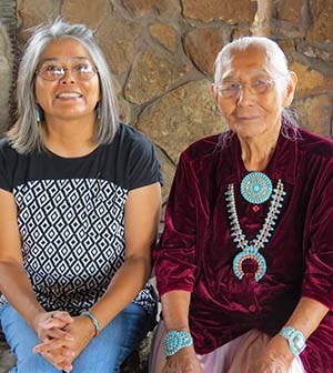 Two Navajo weavers, daughter and mother sitting together and posing for a photo.