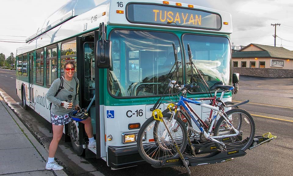 a woman boarding a white and green bus with a rack with two bicycles in front.