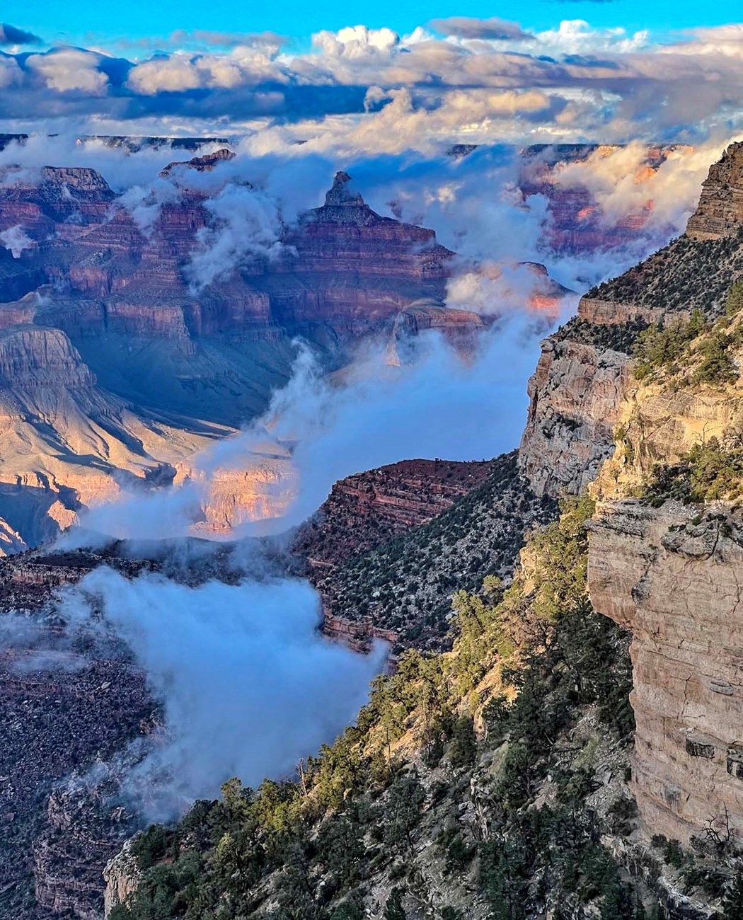 looking down into a vast canyon landscape filled with colorful peaks and cliffs as low hanging clouds crisscross the view.