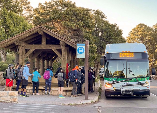 during sunrise, about a dozen hikers are boarding a white and green bue.