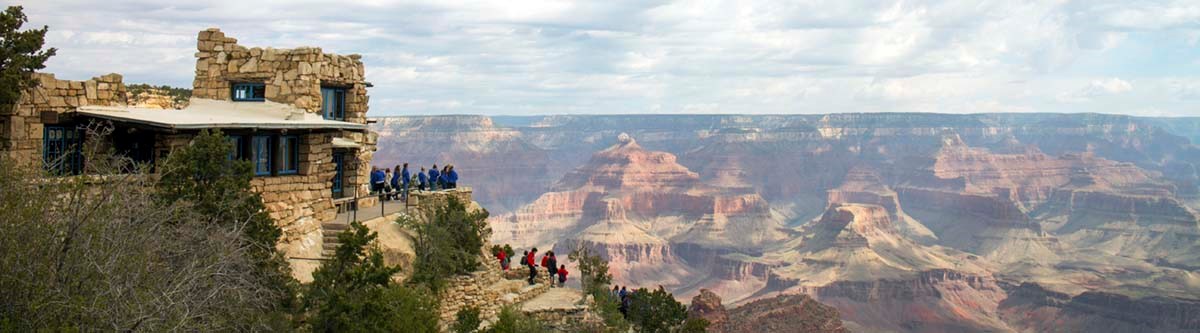 on the left, rustic stone observation building. to the right, a complex landscape of colorful pinnacles and peaks within Grand Canyon