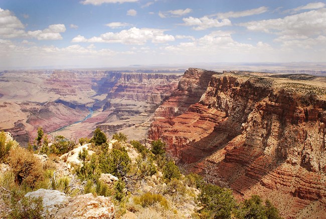 looking down into a canyon with reddish stratified cliffs and a river a mile below.