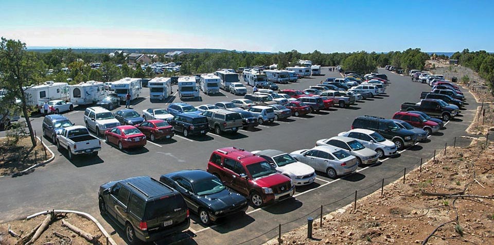 Looking down on a large curved parking lot with 4 rows for cars and a row of large pull-through spaces that are filled with RVs.