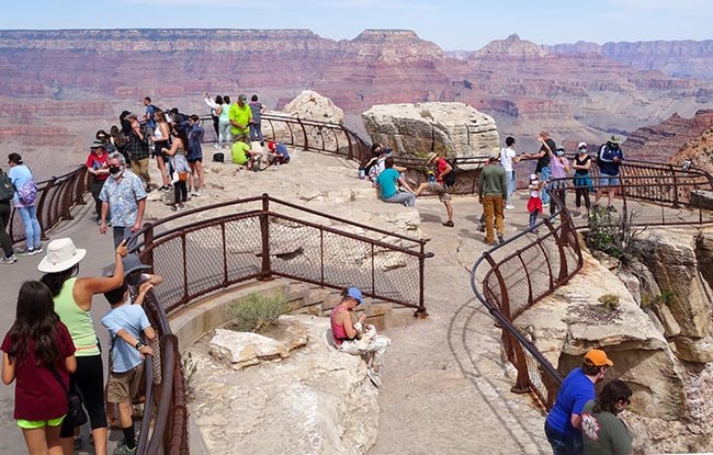 several dozen sightseers scattered around a scenic overlook with metal guard railings around the perimeter of the viewing area.