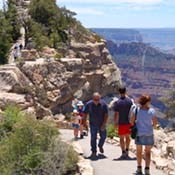 Several day hikers on the paved footpath to Bright Angel Point, North Rim Grand Canyon visible in the distance on the right.