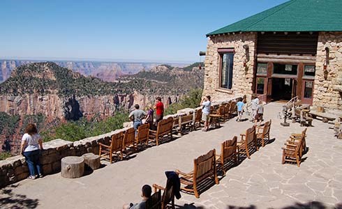 Canyon-facing patio patio of Grand Canyon Lodge. Several people are sitting in chairs enjoying the view.