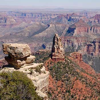 a limestone pillar on the left, and in the distance a pointed peak with sheer sides with a background of colorful rock layers