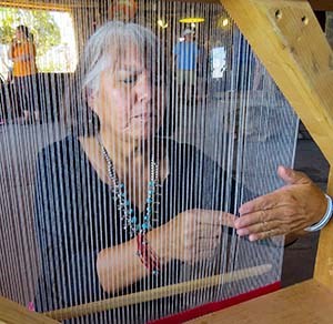 A woman beginning to weave a Navajo Rug as seen through the vertical warps of white yarn