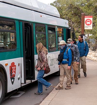aaP1300685 Six personnes portant des masques faciaux et des vêtements d'hiver montent à bord d'un bus vert et blanc.