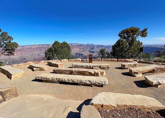 a amphitheater site with three rows of stone benches overlooking a canyon landscape with colorful cliffs in the distance