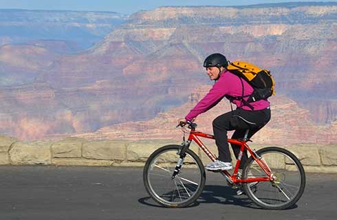 Smiling woman riding a red bicycle along Hermit Road. Grand Canyon beyond.
