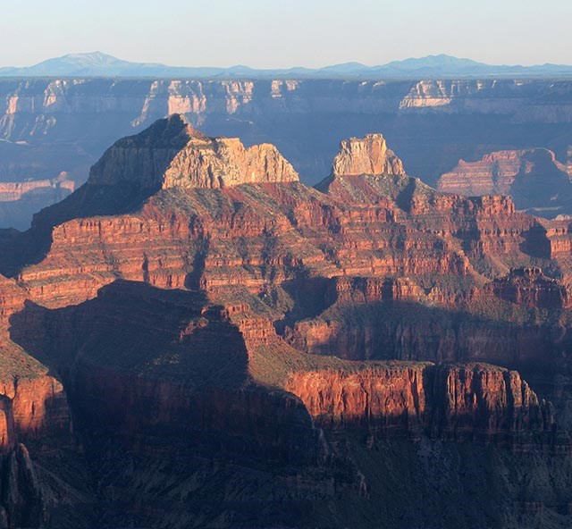 late afternoon light illuminating two connected peaks within a vast canyon landscape