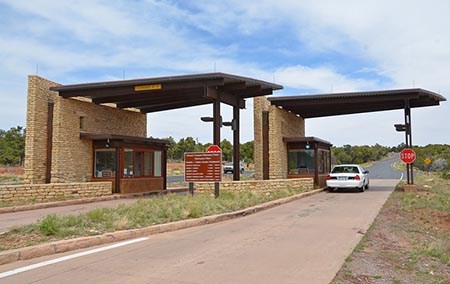 Two lanes leading to an entrance station. The fee booths are built into narrow masonry walls that are 16 feet high. Extending from the walls are roofs that cover the part of the drive-through lanes, where vehicles are alongside the fee booths.