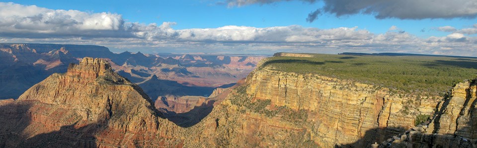 Rising from the floor of a vast canyon, a rugged peak that is connected to the canyon's rim by a v-shaped saddle.
