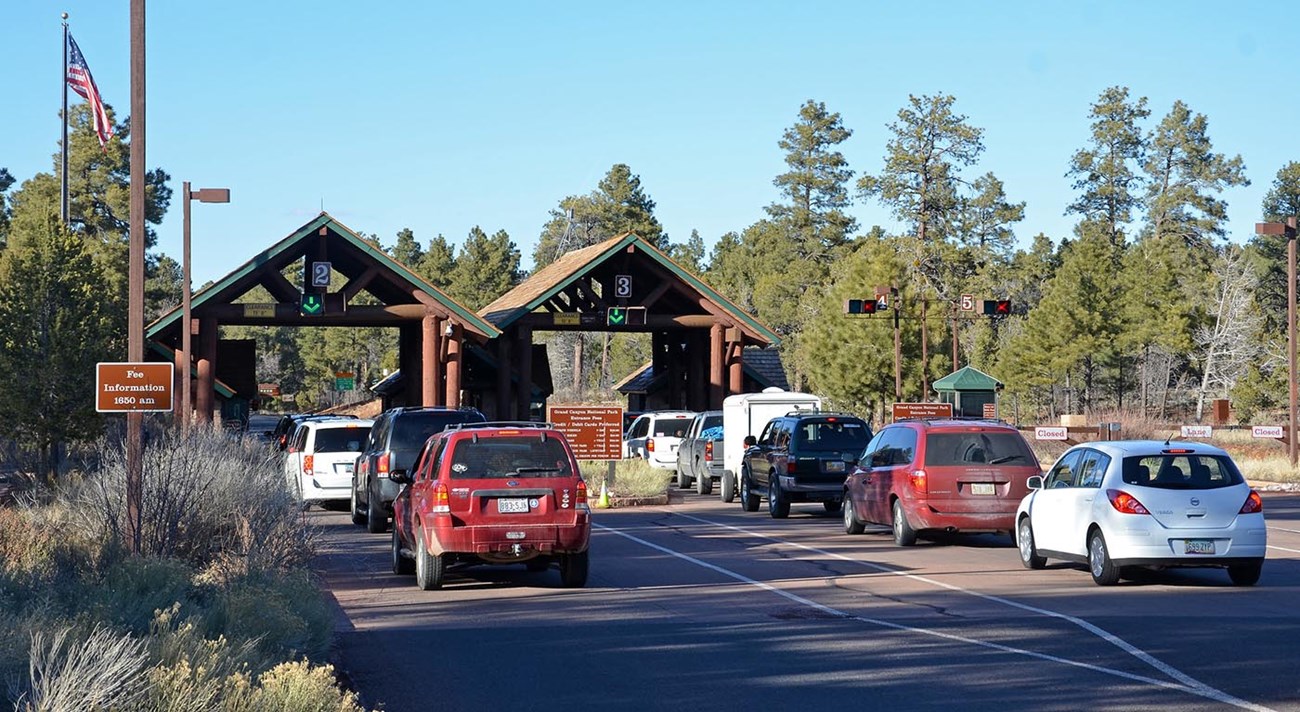 eight cars in two lanes are waiting to enter the park at an entrance station