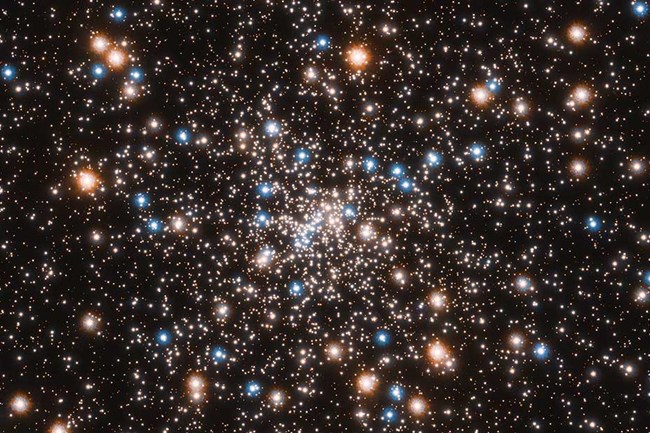 An Ancient Globular Star Cluster appears as scattered orange and blue stars against a black background