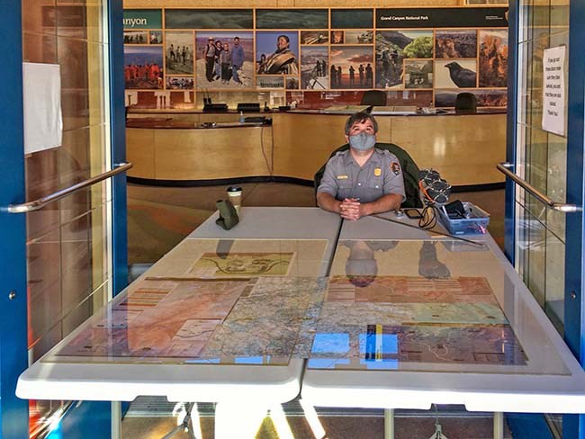 a park ranger is staffing an information table just inside the entrance to a visitor center.