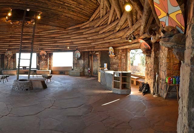 looking acros round Kiva Room of Watchtower. Large picture windows around the circumfrence alternating with stone pillars that hold up a circular log roof. Flagstone floor.