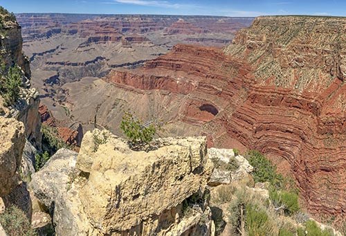 View over limestone pillar at a 3000 foot tall stratified cliff made from layers of reddish rock, with a white cliff above, forming the rim a large canyon.