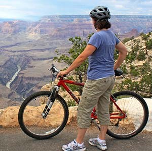 a woman with a red bicycle is standing at the edge of Grand Canyon and looking down at the Colorado River