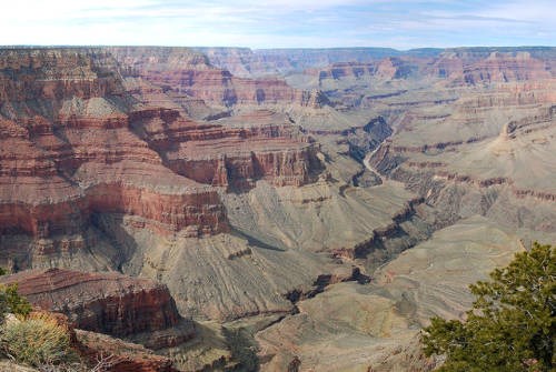 A wide open expanse of a desert canyon with steep, vermilion colored cliffs on both sides and a muddy river within a gorge down below.