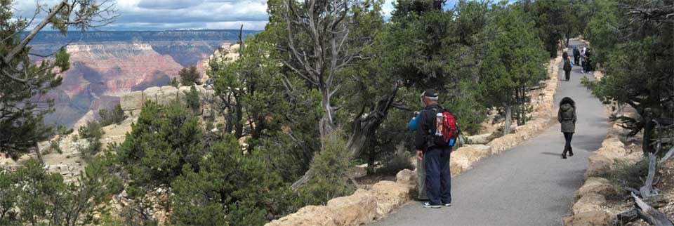 Several people walking along the Canyon Rim Trail on the right. Grand Canyon is visible on the left.