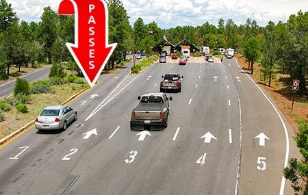 Aerial view showing 5 numbered lanes leading to a park entrance station in a forested area. several vehicles are approaching.