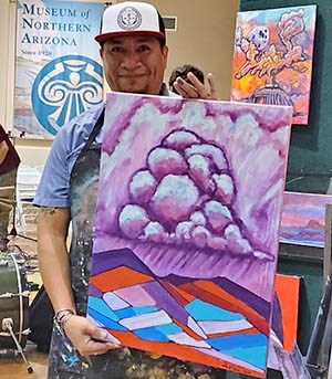 a man standing behind and holding a large painting of stylized thunder clouds above a desert landscape.