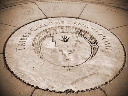 a large circle within a paved area with a stylized symbol of canyon walls. Text reads, "Tribes Call The Canyon Home."