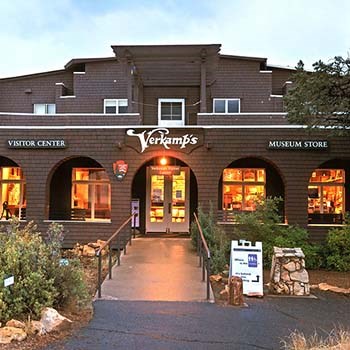 a brown, two-story craftsman-style building. Warm interior light shining through windows at dusk.  