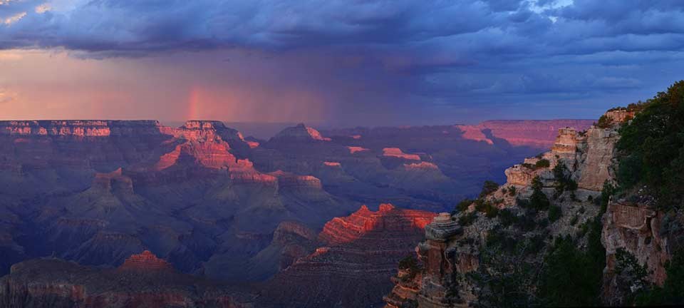 A dramatic red sunset as seen looking east from Yaki Point with stark blue clouds and a trace of a rainbow.