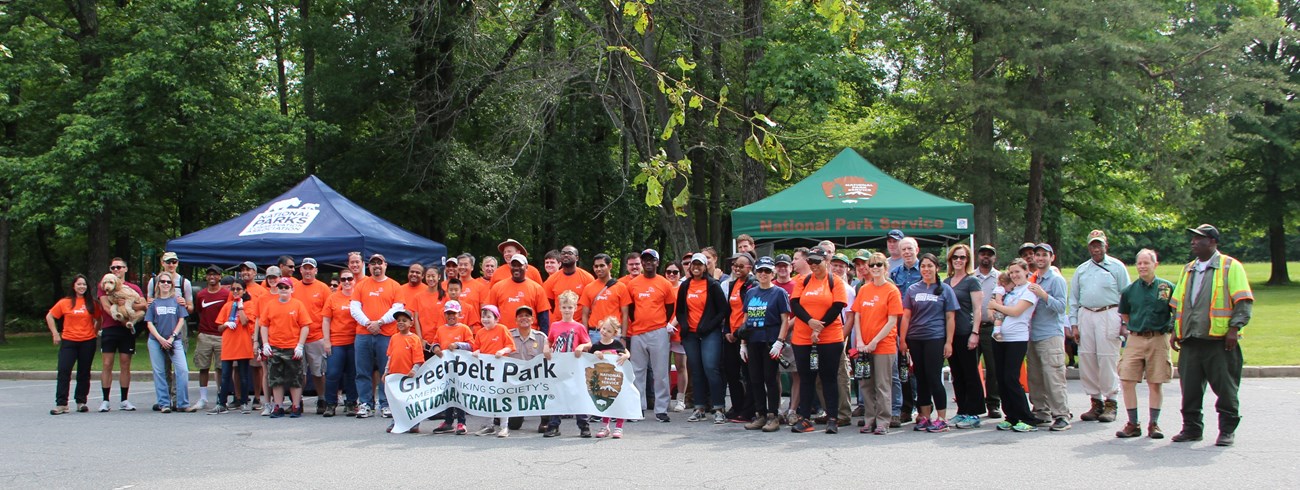 75 Greenbelt Park volunteers holding a National Trails day sign with 2 tents in the background