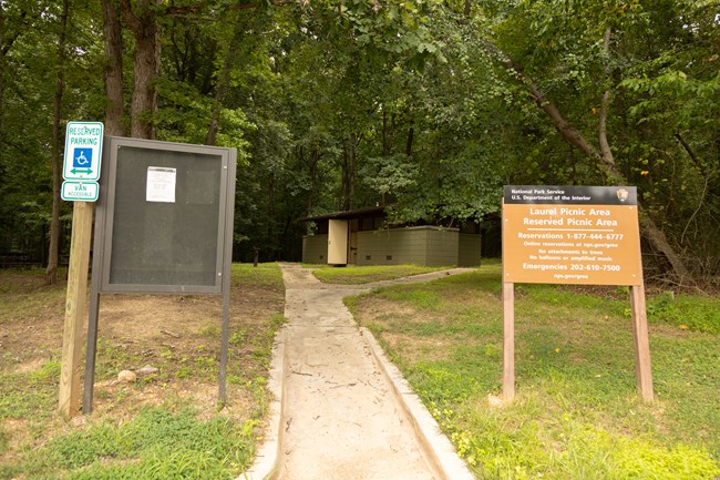 Two signs stand on either side of a paved sidewalk, eventually leading to a comfort station