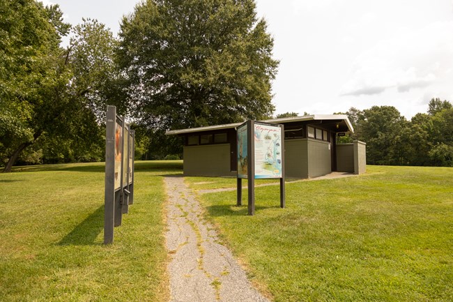 A paved road with cracks leads to waysides and eventually a comfort station in a picnic area