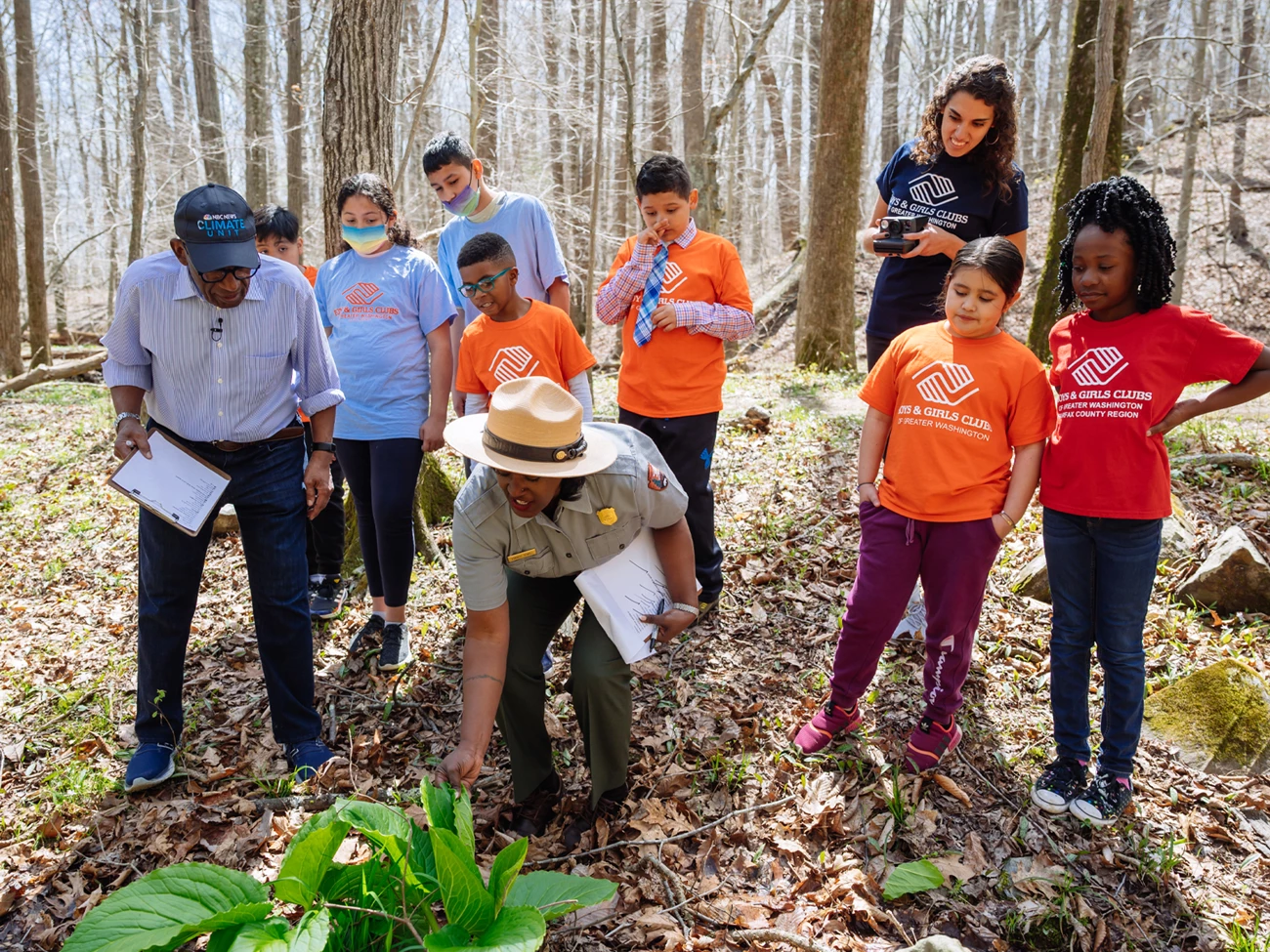 Field trip at Great Falls 2021 Ranger bends over to touch large leafed plant on ground while kids and chaperones watch.