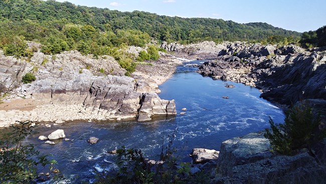 A long deep blue river channel down the center with tall rocky cliffs and tall trees on both left and right sides.