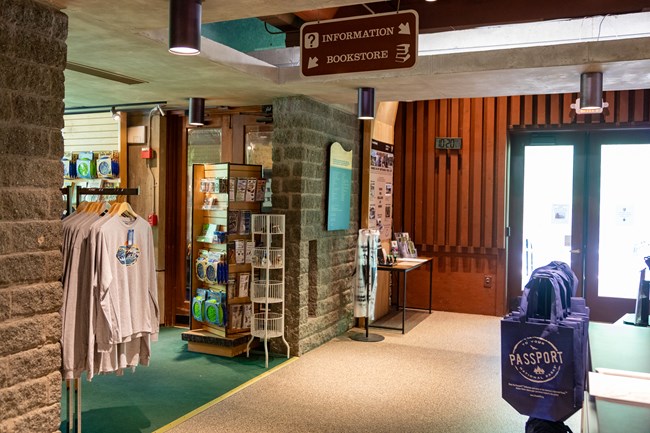 A rack of t-shirts and displays of souvenirs across from a counter near glass double doors.