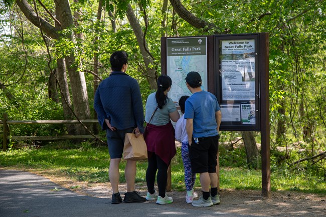 Four visitors read a bulletin board with a map on a sidewalk.