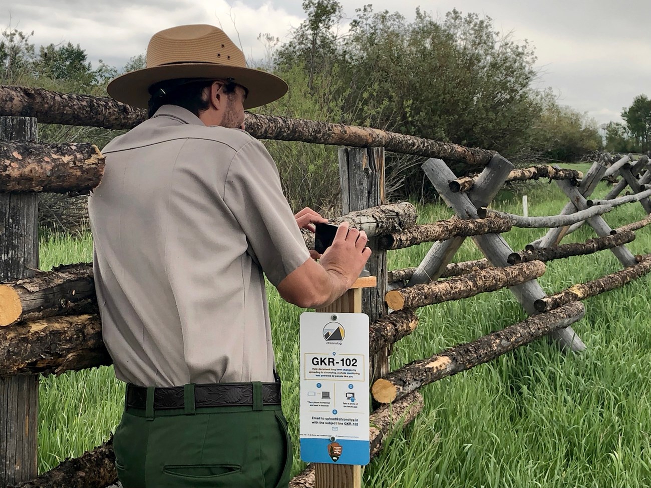 Park ranger holds a cell phone in bracket mounted on post with sign giving instructions
