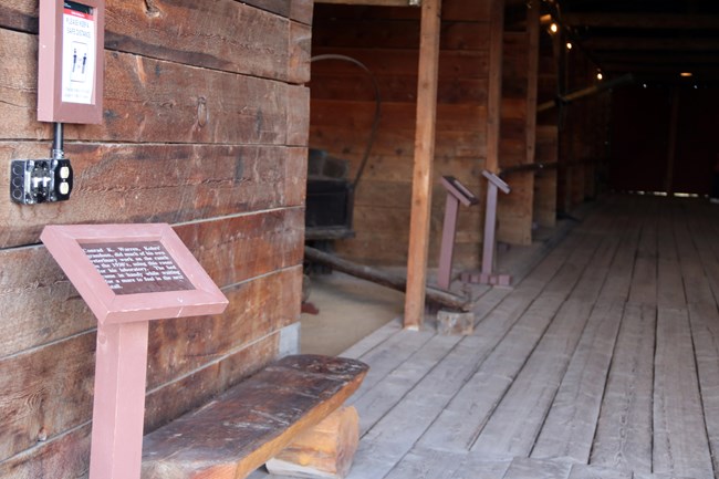 Inside a barn with wooden walls and floors, 3 exhibit signs are shown down the length of the barn with a wagon partially visible in middle left